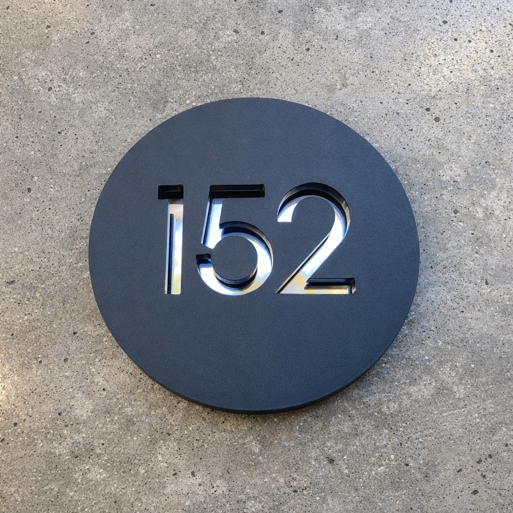 Round house number sign with '152' on a concrete surface