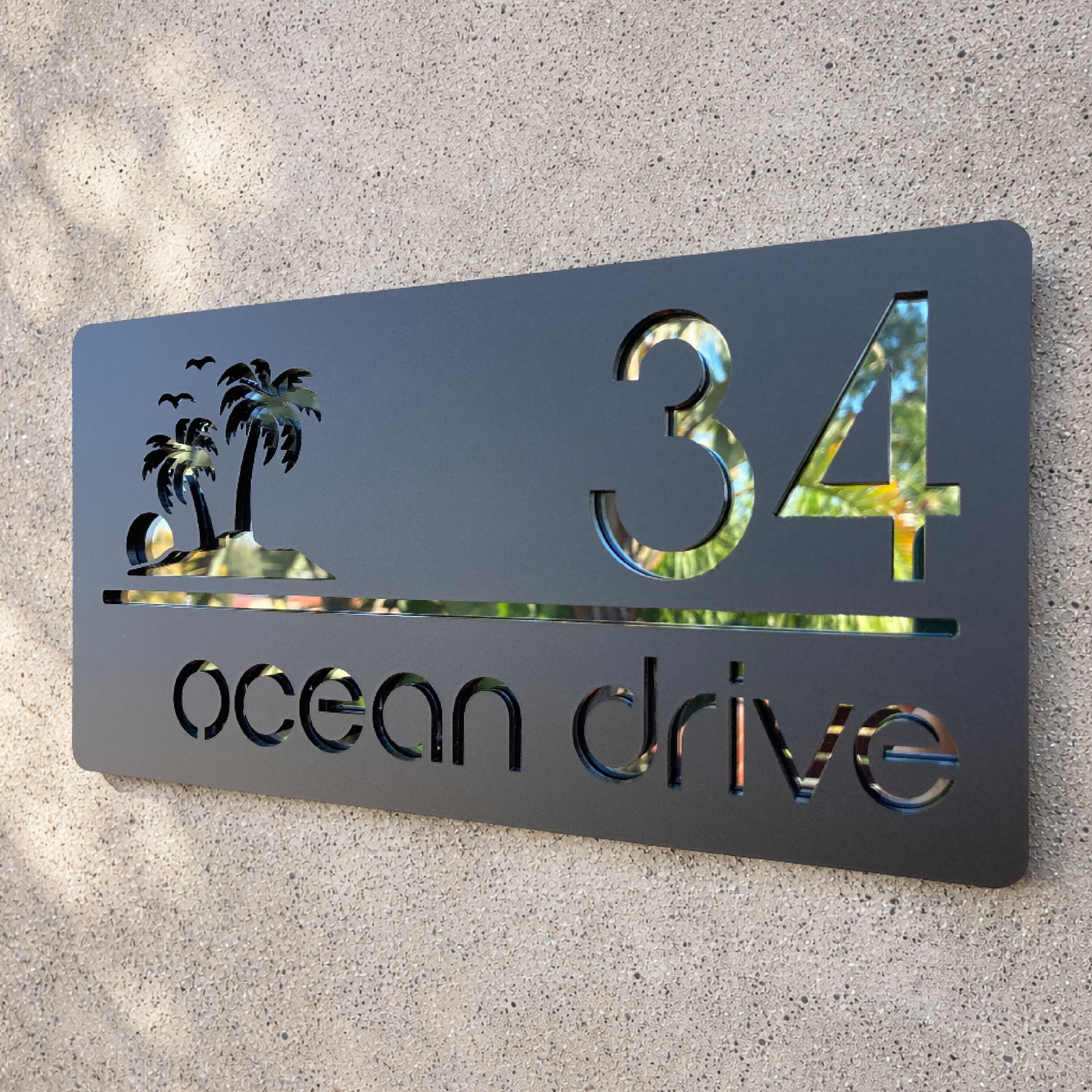 Metal house number sign with palm trees and '34 ocean drive' on a textured wall.