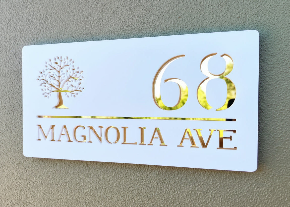 White house number sign with gold text '68 Magnolia Ave' on a beige wall.