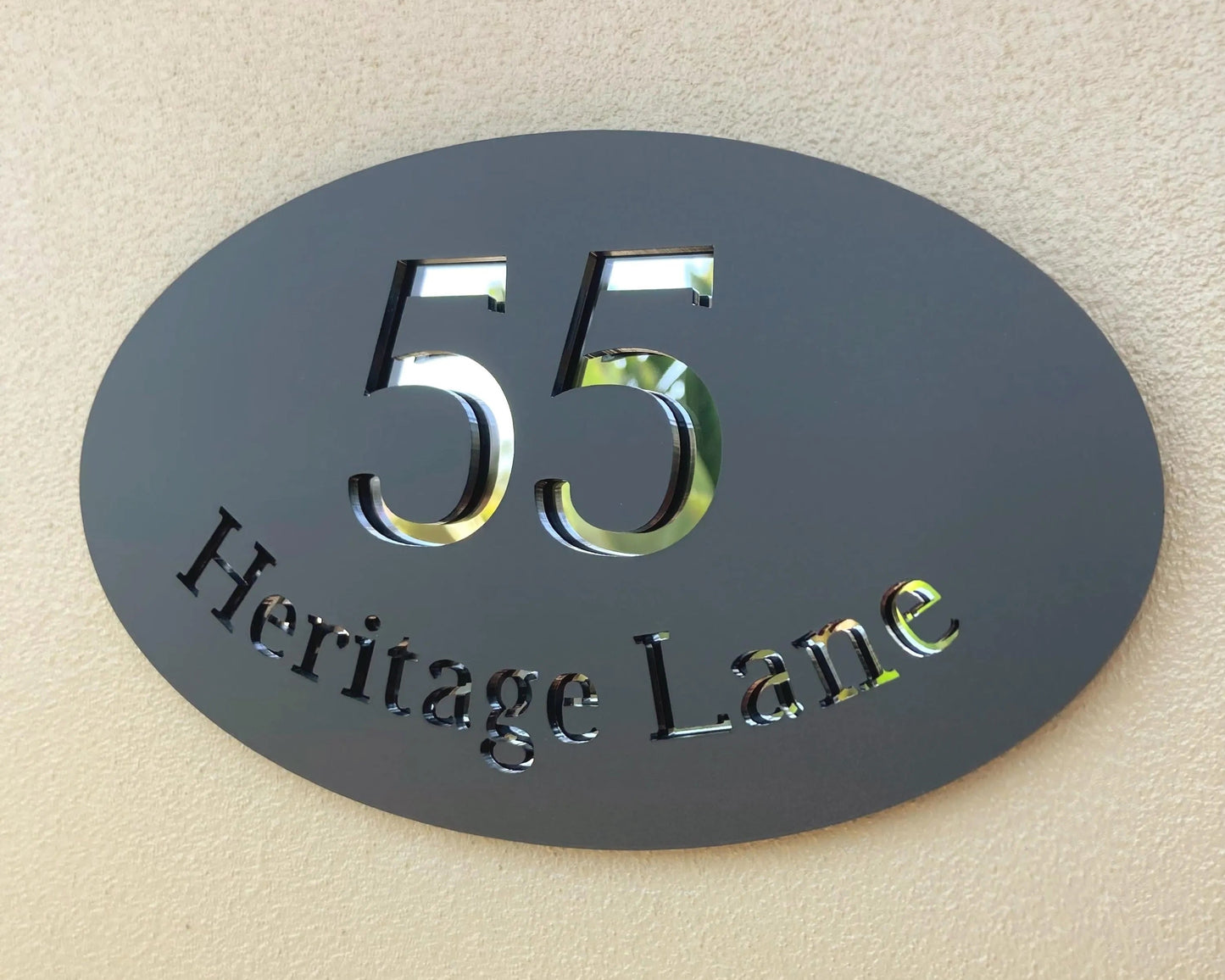 Oval-shaped house number sign with '55 Heritage Lane' on a beige wall.